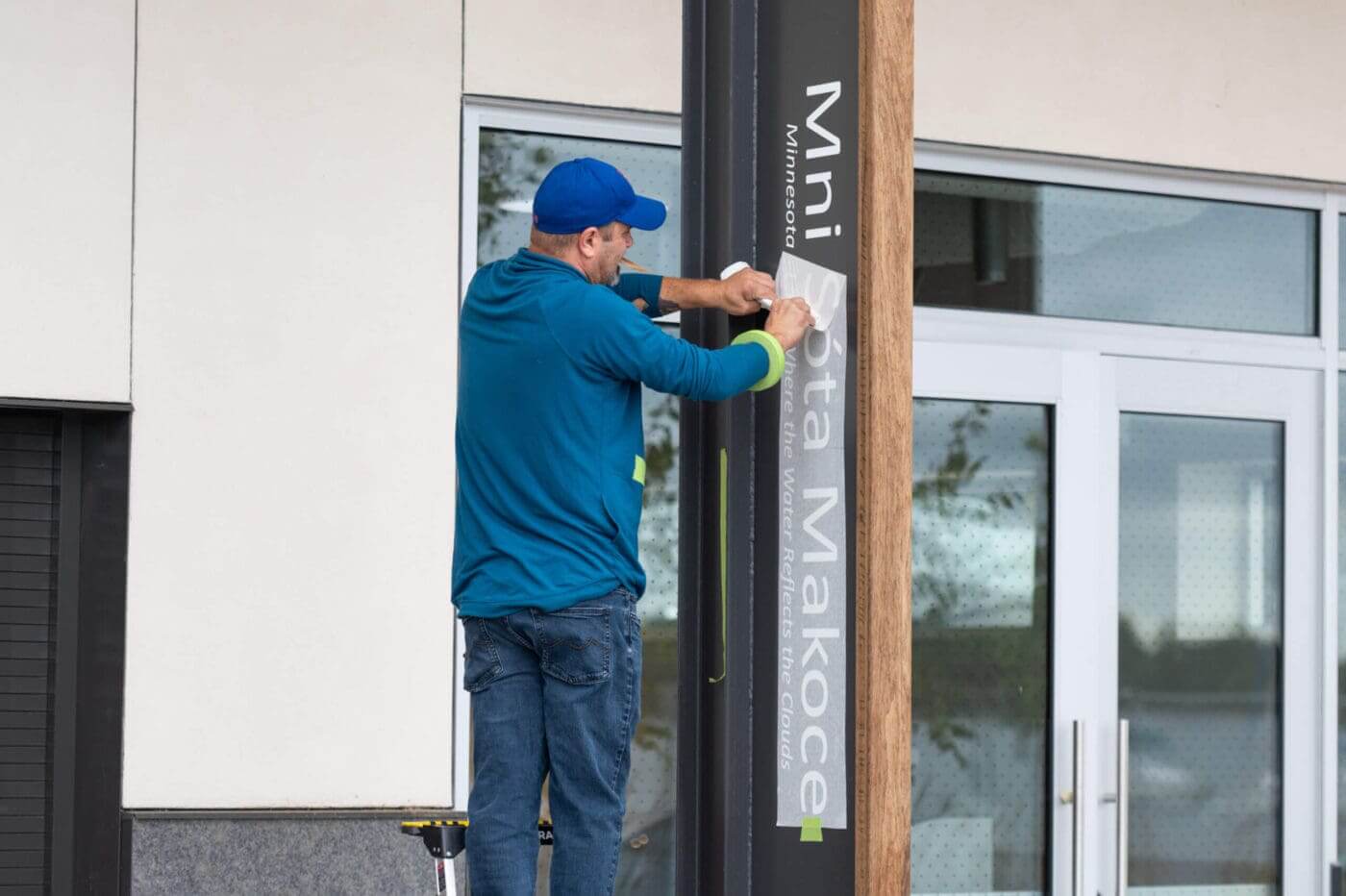 A man installs Dakota language decals at the new Bde Maka Ska Pavilion