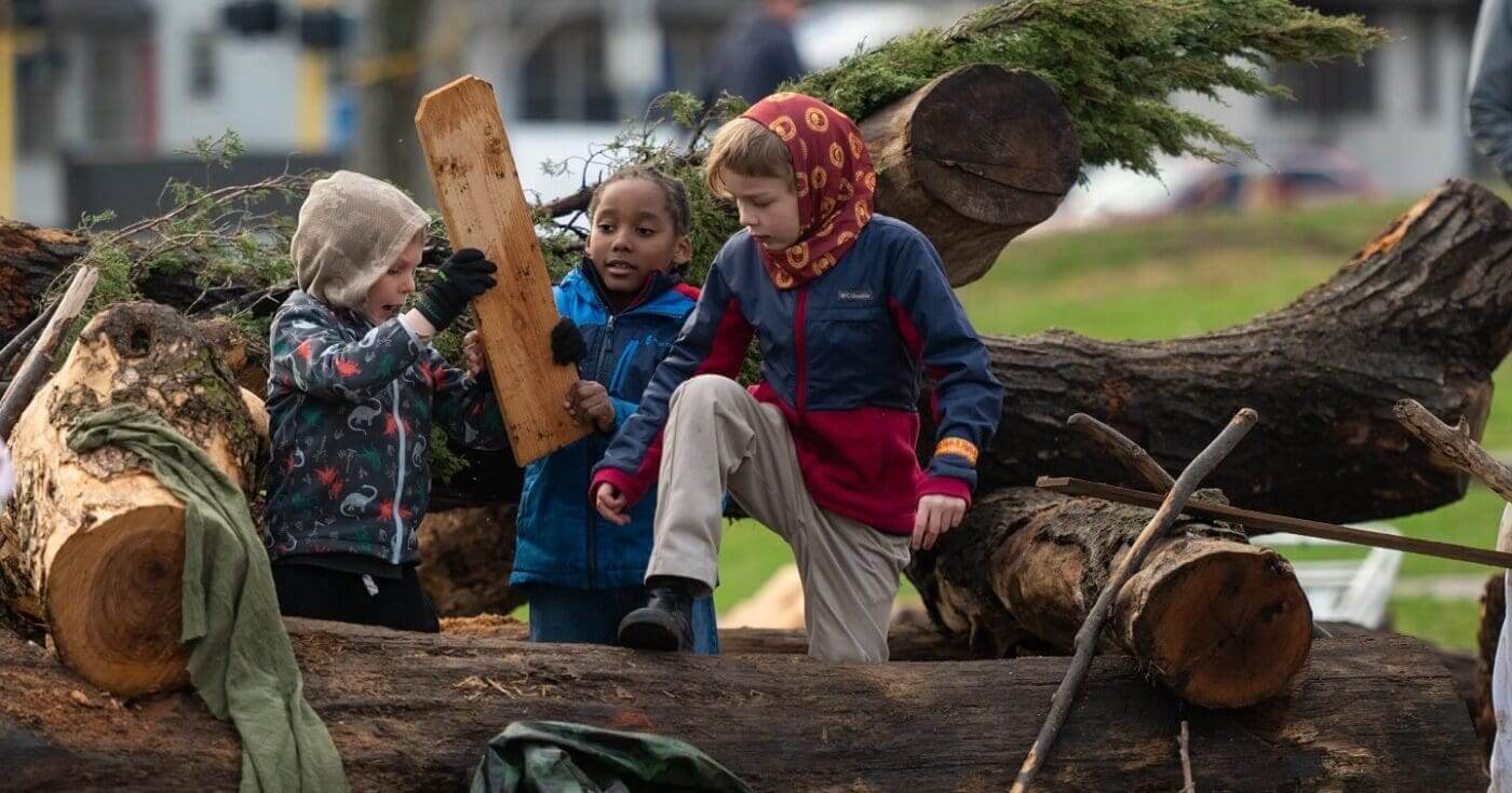 Kids play with logs and wood in the nature play area during the 2023 Minneapolis Arbor Day Celebration at Windom Northeast Park