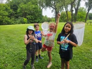 Four kids in a park with bug nets and magnifying classes