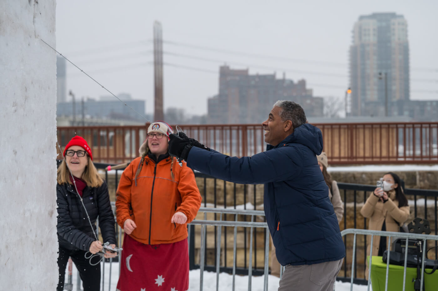Three people work a wire saw to cut the first chunk off a large cube of snow that will become a snow sculpture