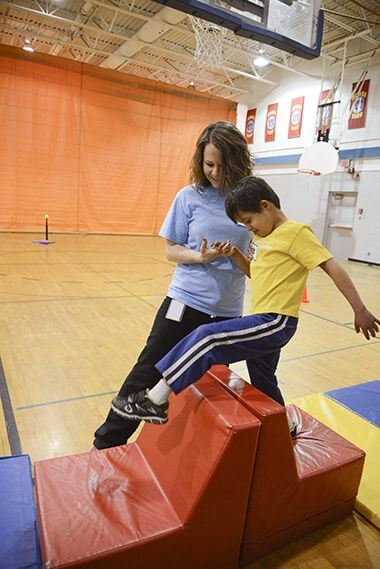 Instructor Spotting Child on Adaptive Obstacle Course