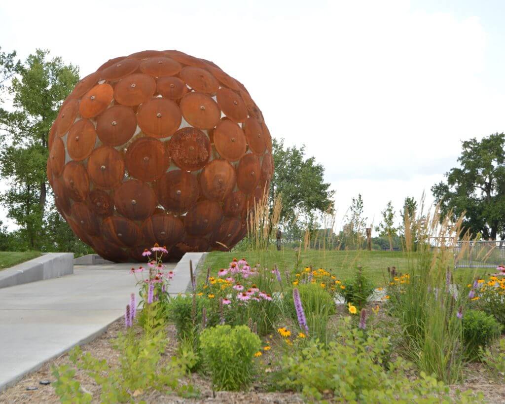A large, spherical, iron sculpture and flowers at Sheridan Memorial Park
